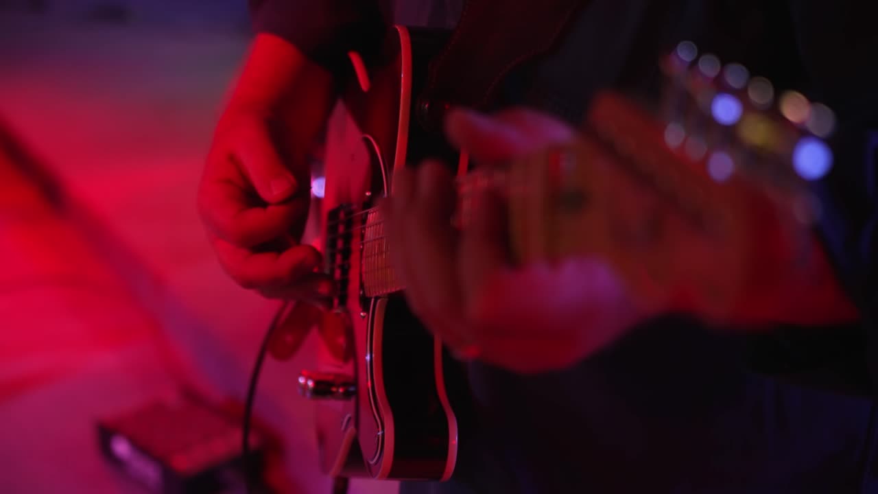 Chitarrista uomo che suona accordi, suona la chitarra elettrica su un palco illuminato di rosso, primo piano in slow motion 4K.