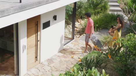 video de una feliz pareja diversa que llega con una maleta a la puerta de una casa de vacaciones soleada