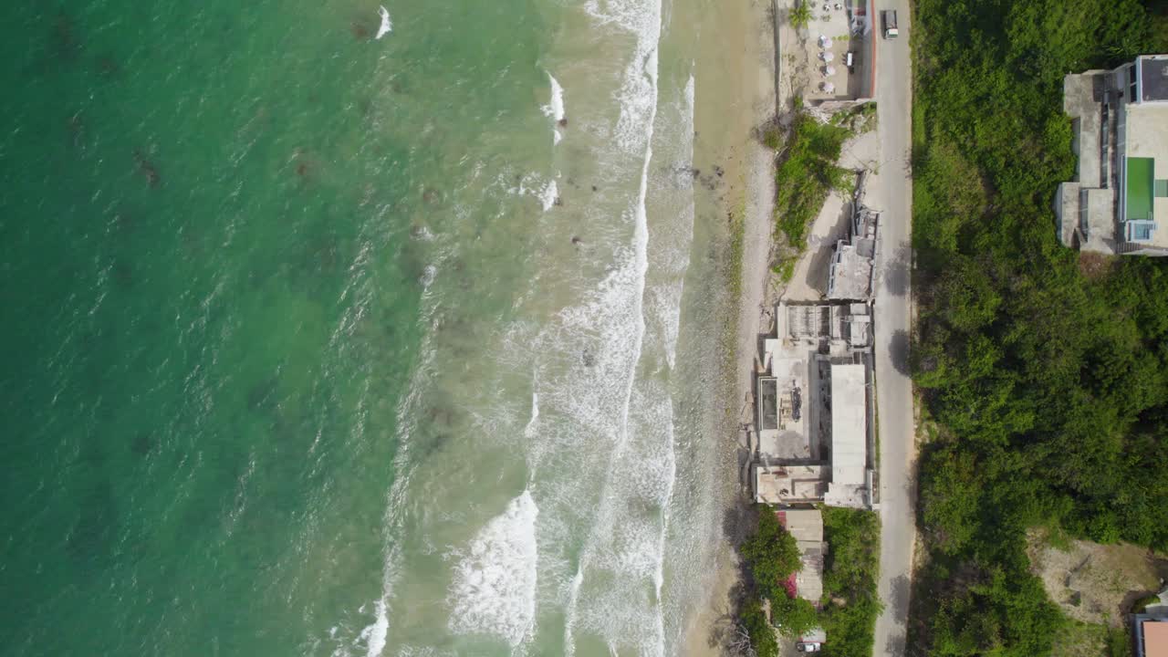 Aerial tracking shot over a Caribbean beach, showcasing clear waters, sandy shores, and a car driving by