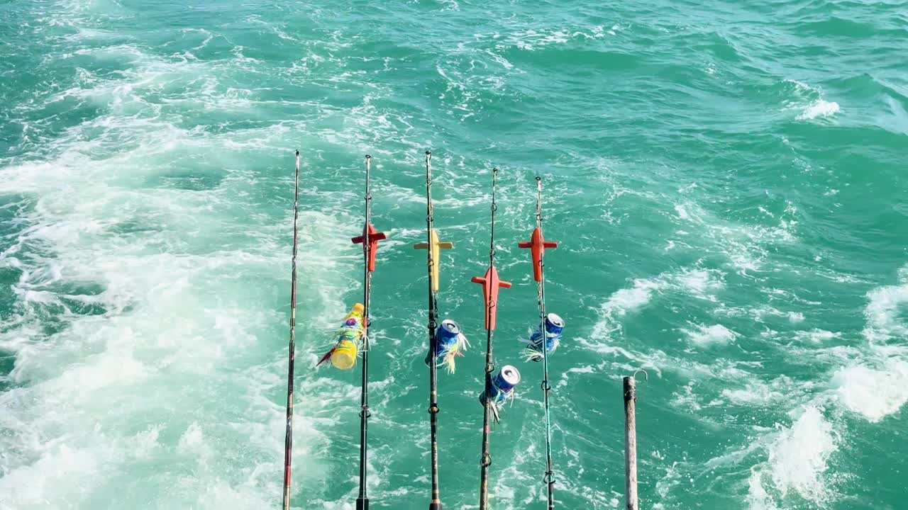 Fishing rods on a boat in Phuket, Thailand, with ocean wake and vibrant turquoise water under bright daylight