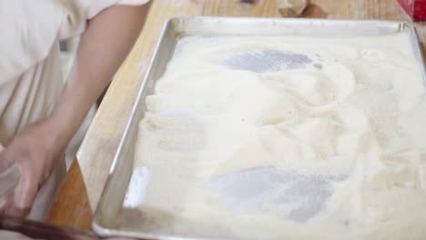 primer plano de un chef masculino cubriendo rosquillas con azúcar en una cocina de panadería