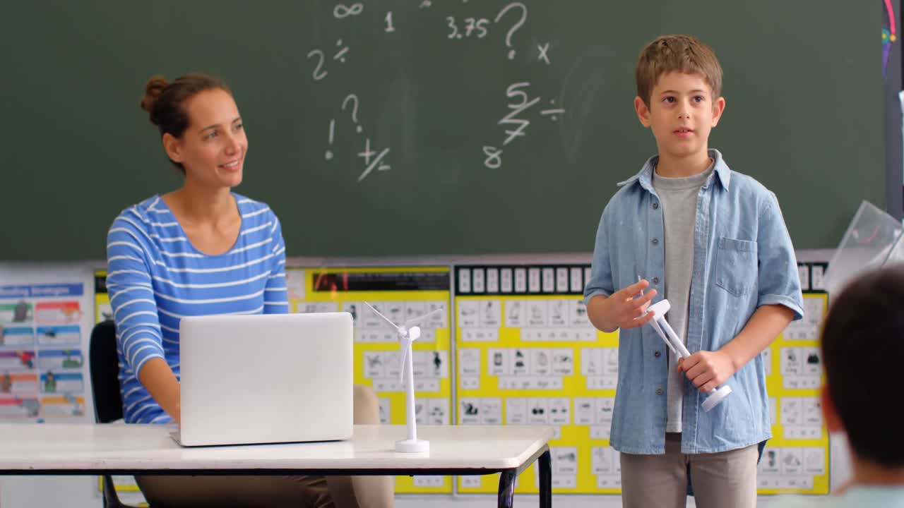 vista frontal de un escolar caucásico explicando sobre el modelo de molino de viento en el aula 4k