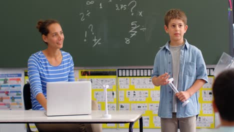 front view of caucasian schoolboy explaining about windmill model in the classroom 4k