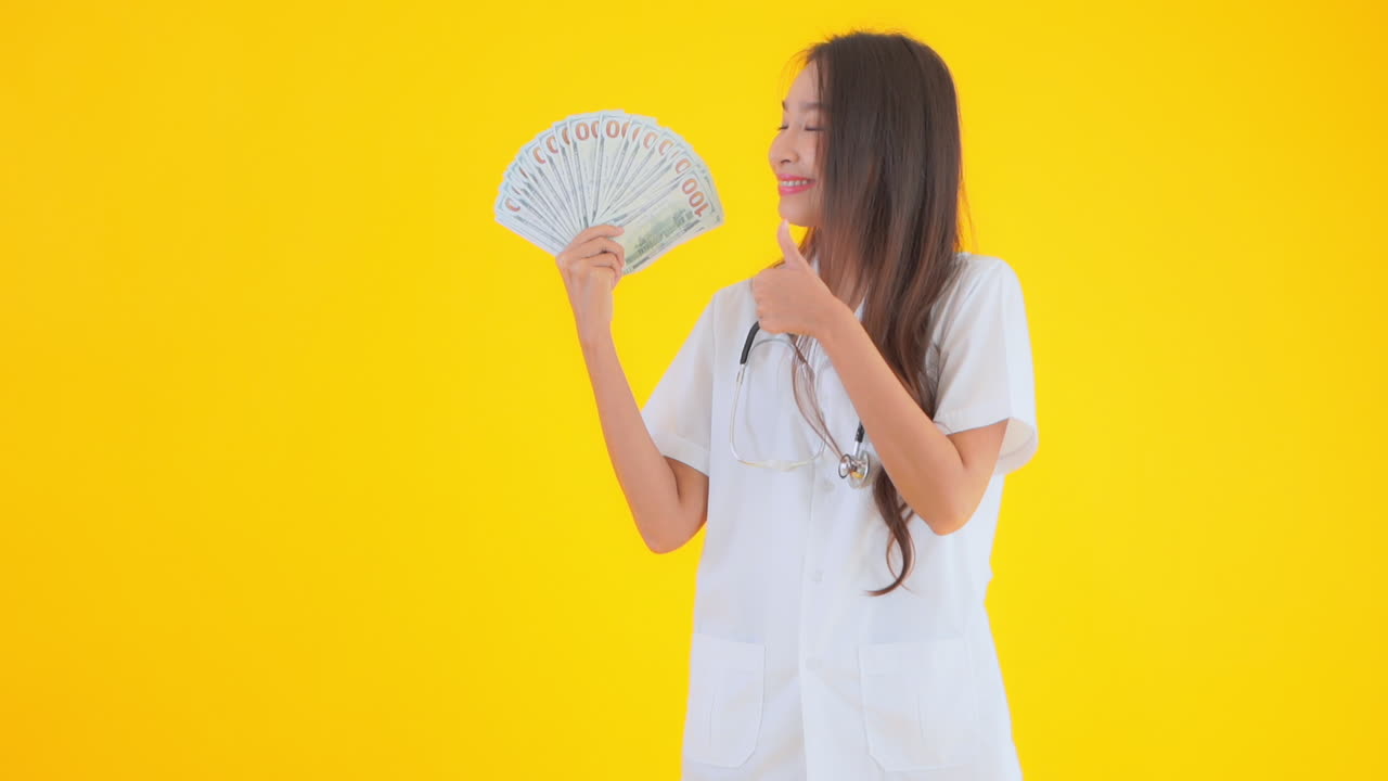 เจ้าหน้าที่ทางการแพทย์หญิงถือพัดที่ทำจากธนบัตรหนึ่งร้อยดอลลาร์ขึ้นมาที่ระดับใบหน้า มีพื้นที่ส าหรับใส่ข้อความ