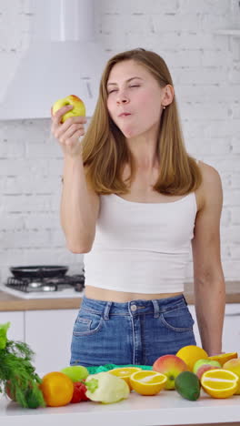smiling housewife at home. sporty young woman eating healthy food in light kitchen. vertical video