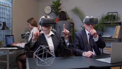 Elderly-old-man-boss-with-woman-colleague-wearing-virtual-reality-glasses-tries-3D-app-for-VR-helmet