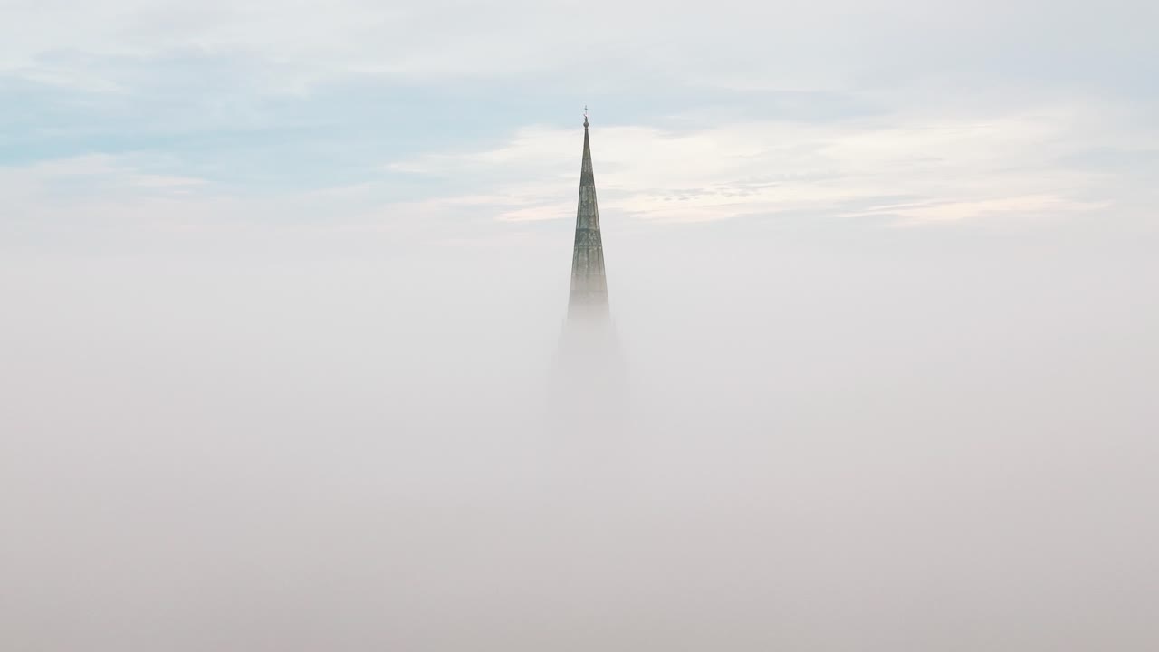 Droneoptagelse fra luften af Salisbury Katedrals spir, der dukker frem gennem morgentåge og dis over byen Salisbury i Wiltshire, England.