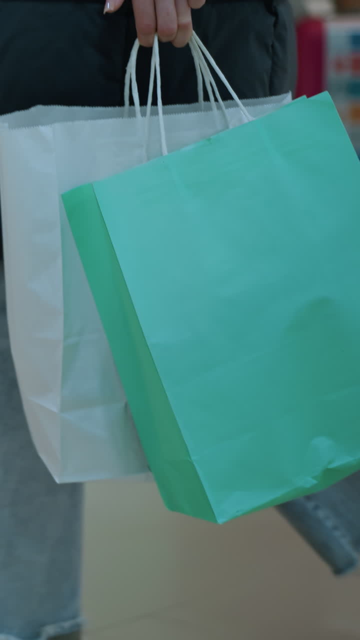 vista lateral de una persona caminando por el espacio comercial en un centro comercial bien iluminado llevando bolsas de compras, maniquín vestido con ropa y bolsas de viaje coloridas dispuestas dentro de una pantalla de vidrio