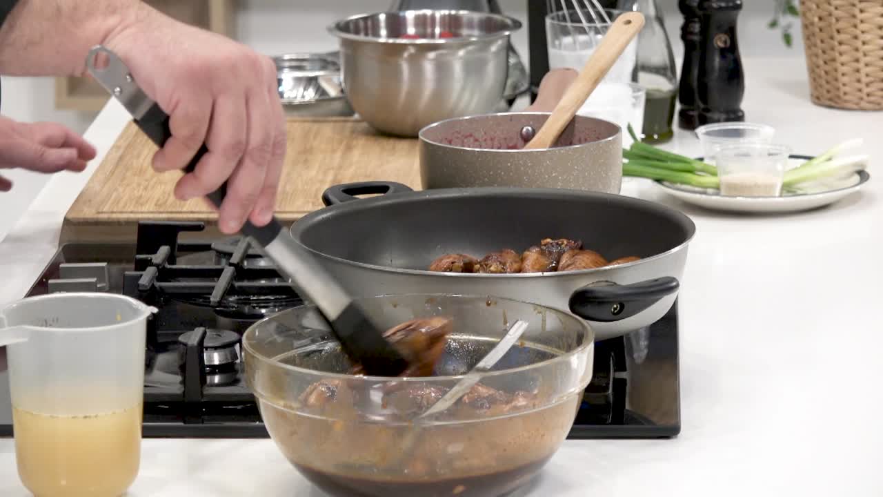 A chef skillfully prepares chicken pieces, tossing them in a flavorful marinade while cooking on a stovetop. Fresh ingredients and kitchen tools are prominently displayed