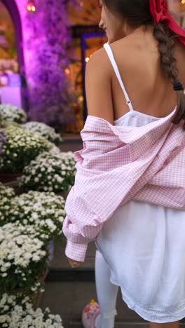 young woman in pink shirt and white dress near flowers