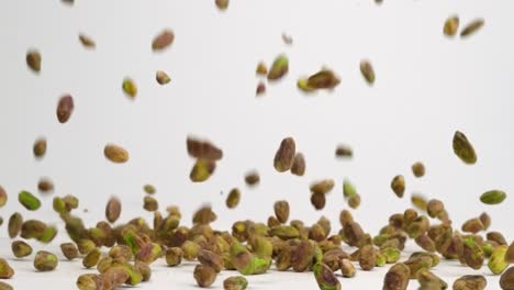 shelled pistachio nuts raining down on white table top and bouncing into a pile in slow motion