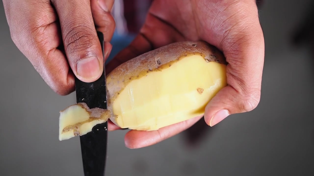 Persona che sbuccia una patata cruda con un coltello da cucina