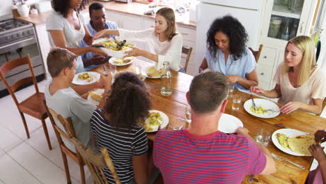 dos familias con niños adolescentes comiendo comida en la cocina