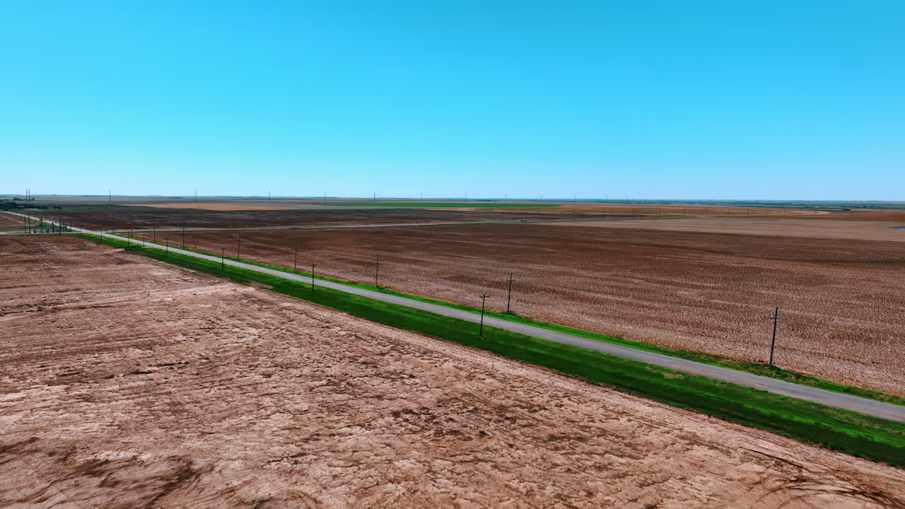 Asphalt road with green grass around crossing the vast field with no vegetation. Drone footage above the dry deserted lands.