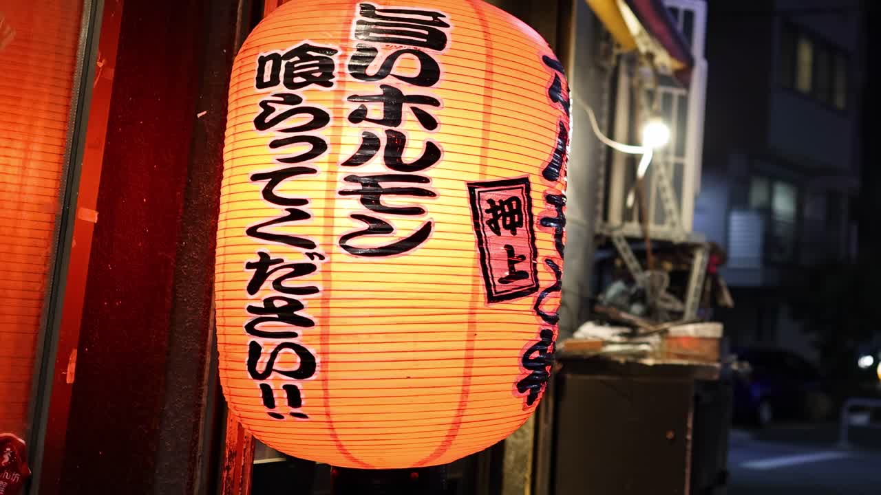 A glowing lantern with Japanese characters, casting warm light in an urban setting.