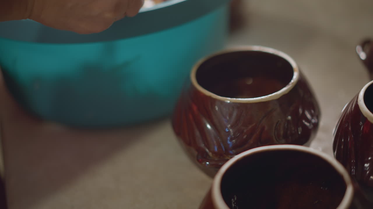 Preparazione di una pentola di terracotta con ripieno tritato. Mani che porzionano il composto condito in un recipiente di ceramica. Scena di preparazione in cui le mani riempiono la pentola di terracotta con ingredienti tritati e conditi da una ciotola.