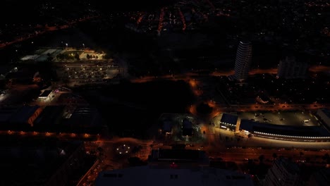 drone glides over estimar hotel in calpe at night, with glowing windows, pool lights, and the coastline illuminated under a starry sky.