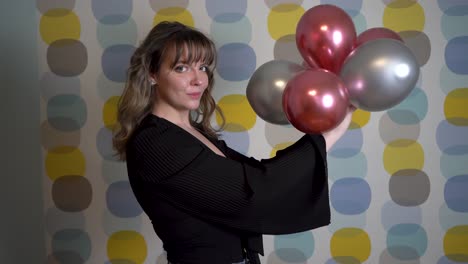 mujer joven posando y sosteniendo globos en la mano contra un fondo colorido