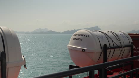 View from a ferry in Koh Samui, Thailand. Life preservers rest on the deck as the sea and distant mountains create a serene and picturesque journey.