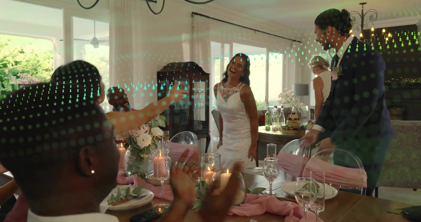 Convidado mais velho entregando buquê, conduzindo noiva e noivo à mesa da recepção do casamento, com convidados aplaudindo.