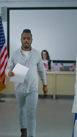 African-American-man-takes-paper-ballot-from-female-polling-officer-at-polling-station-and-walks-to-voting-booth.-National-Election-Day-in-the-United-States-of-America.-Civic-duty-and-democracy.