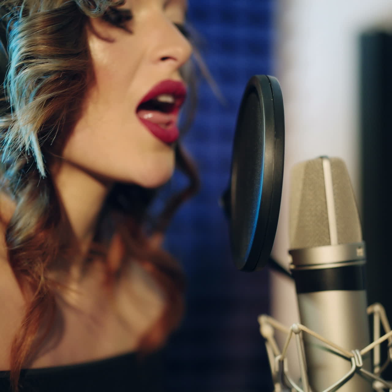 Vinnitsa, Ukraine - May 2019: Young woman recording a song in a professional studio. The girl sings into the microphone.