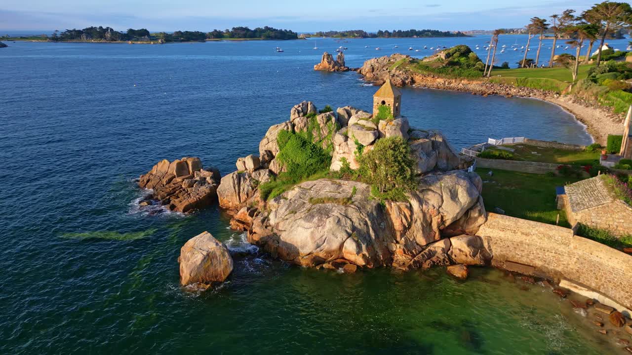 La Sentinelle oratory on rocky peninsula in Port Blanc, overlooking beautiful bay with clear water and sandy beach in Brittany, France. Aerial drone at low altitude