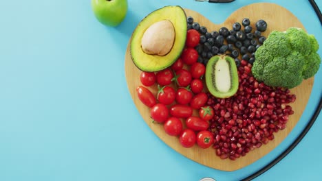 Video-of-stethoscope-and-fresh-fruit-and-vegetables-on-heart-shaped-wooden-board-on-blue-background