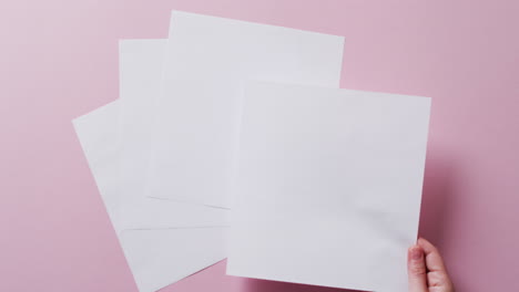 mano sosteniendo un pedazo de papel sobre pedazos de papel con espacio de copia en fondo rosa en cámara lenta