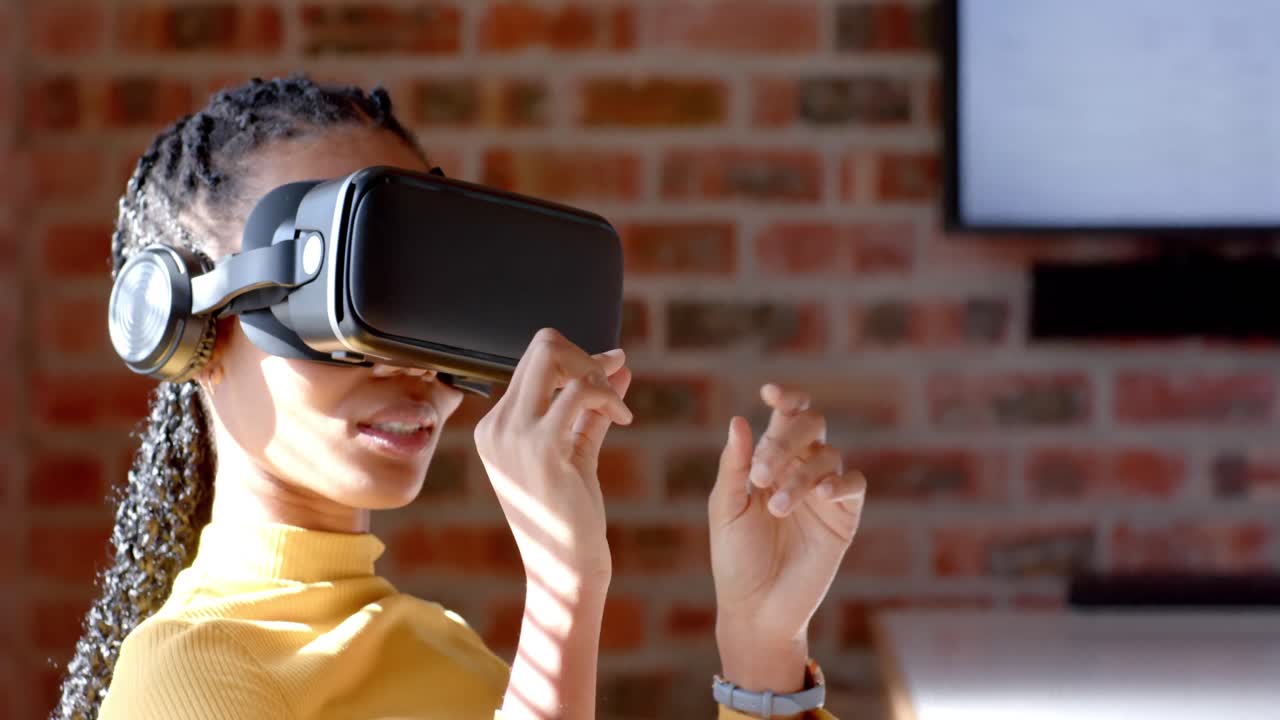 Afrikansk-amerikansk afslappet forretningskvinde bruger VR-headset på et solrigt kontor, slow motion.