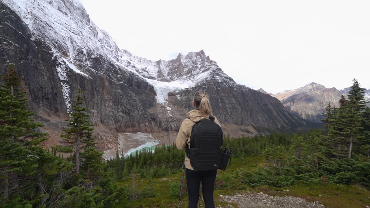 mujer nórdica caminando por el sendero deteniéndose para mirar el glaciar lejano, el monte edith cavell