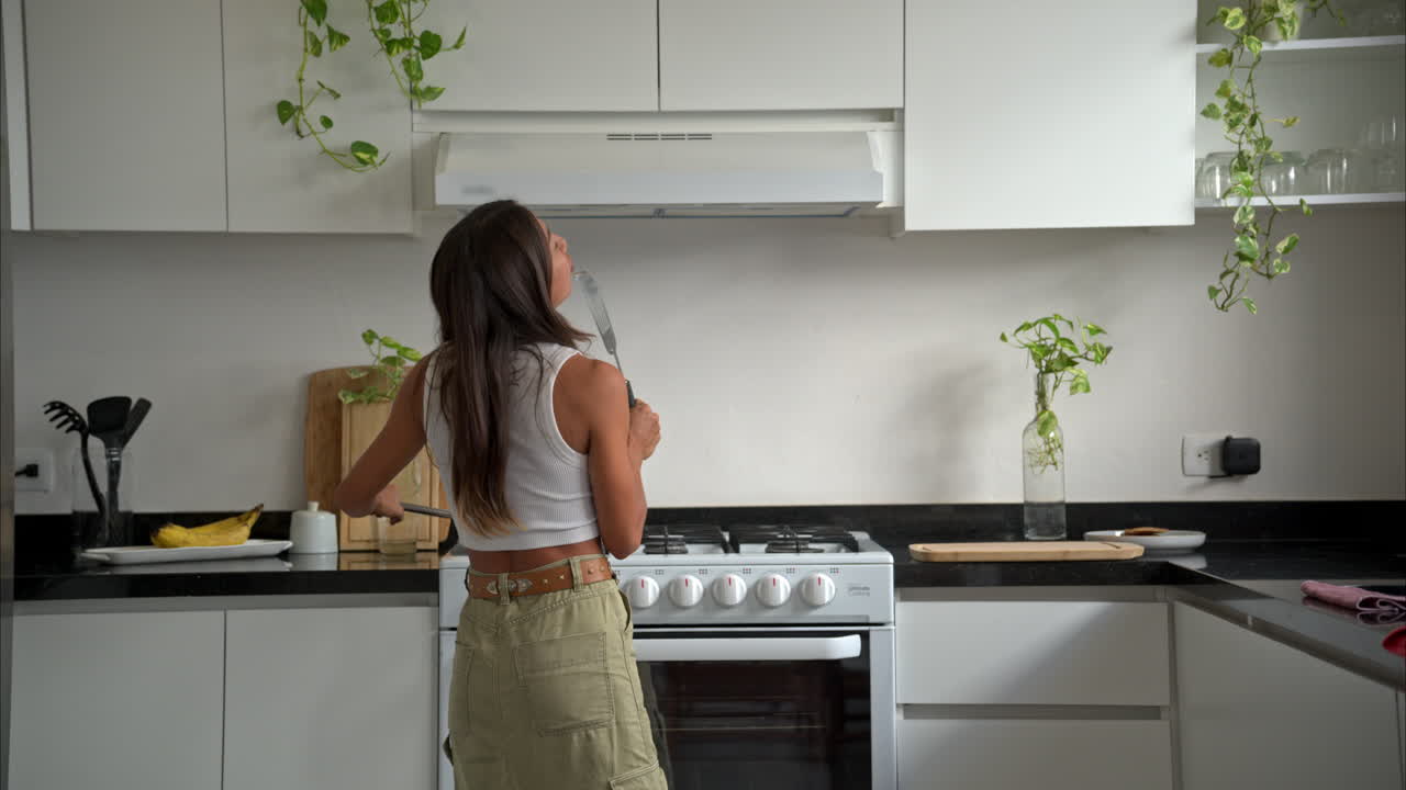 Rallentatore di una donna latina messicana bruna e in forma che cucina, ascolta una canzone, balla e canta, godendosi un bel momento da sola.