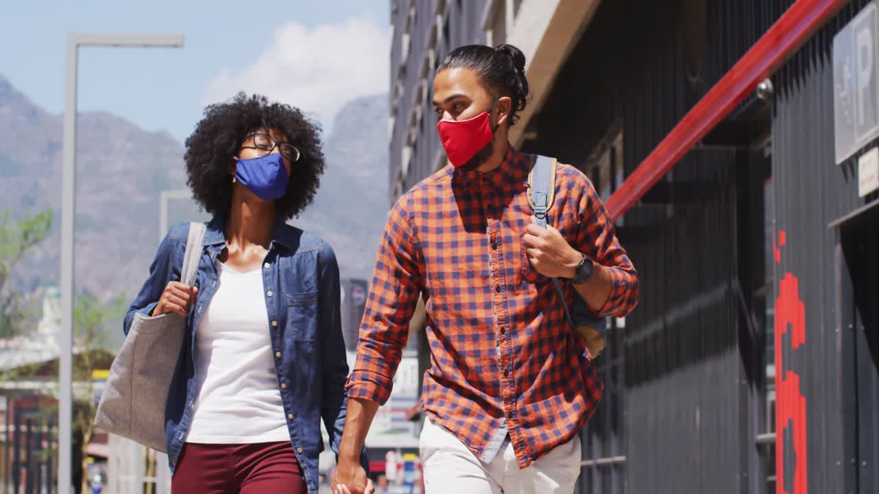 Diverse couple wearing face masks walking and holding hands