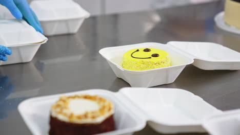Packaging the ready-made sweet desserts in individual boxes. Hands in latex gloves put down the lids of packages. Close up.