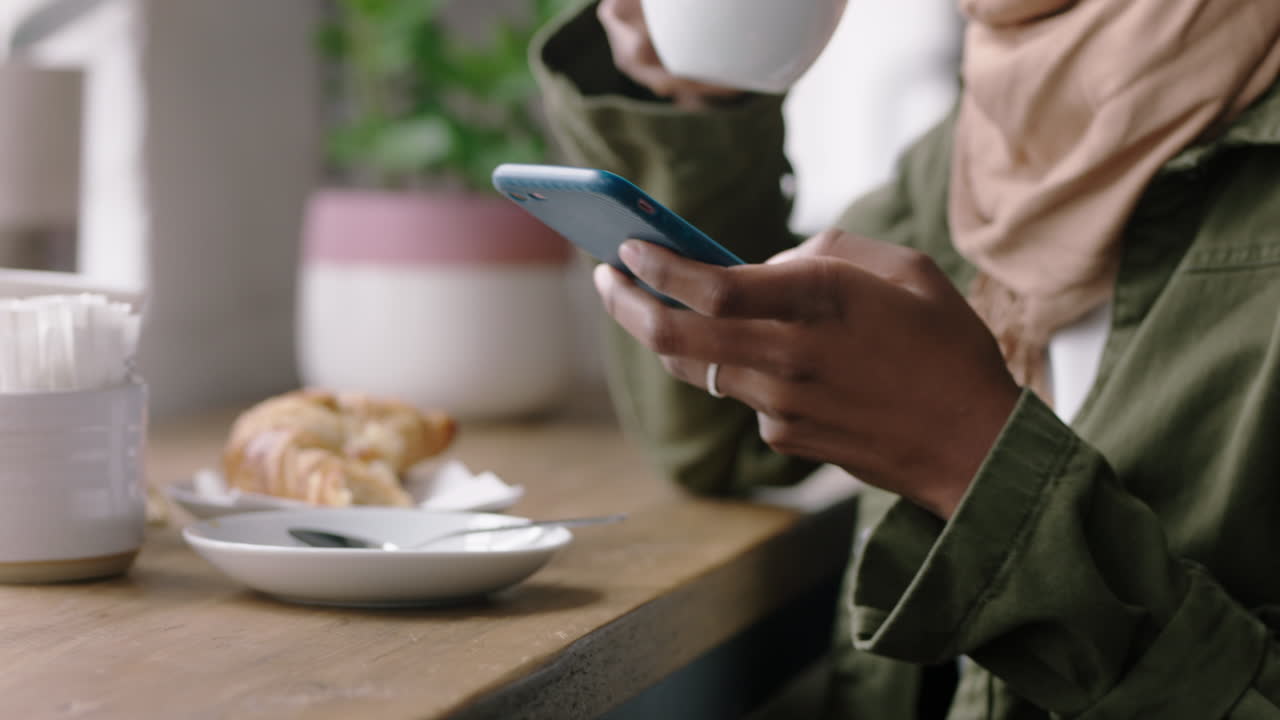 mujer de negocios musulmana usando un teléfono inteligente en un café navegando por mensajes en línea bebiendo café enviando mensajes de texto compartiendo estilo de vida en las redes sociales disfrutando de la comunicación por teléfono móvil de cerca manos