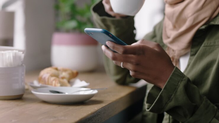 muslim business woman using smartphone in cafe browsing online messages drinking coffee texting sharing lifestyle on social media enjoying mobile phone communication close up hands
