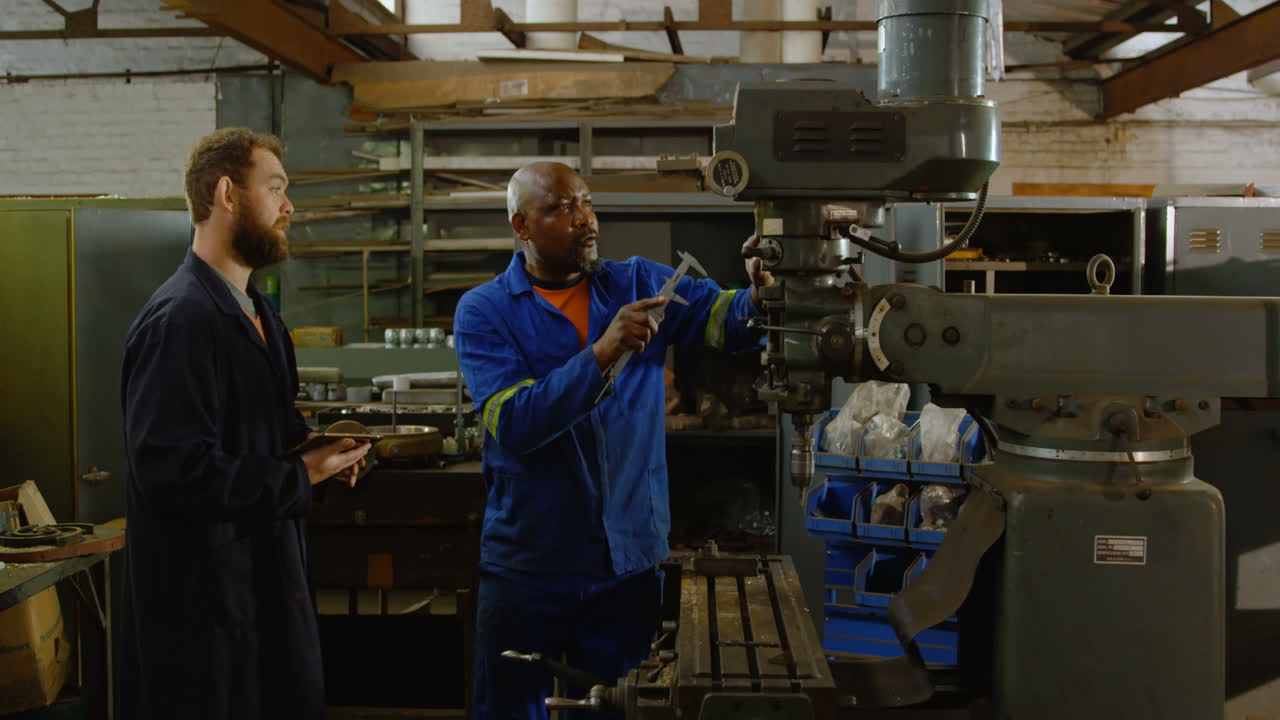 Two metalsmiths discussing over machine 4k