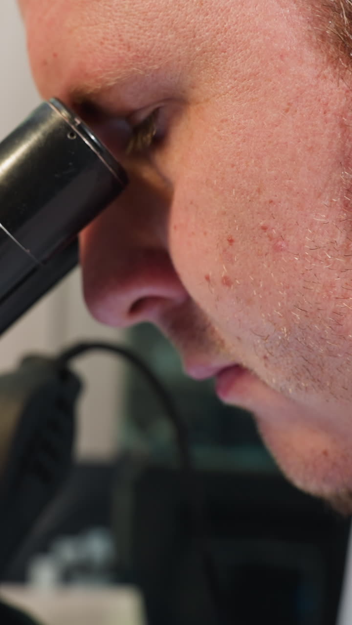 una vista de cerca de un técnico enfocado usando un microscopio en un entorno de laboratorio, luego retiró sus ojos del microscopio