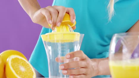 mujer preparando jugo de lima dulce de un exprimidor contra un fondo violeta
