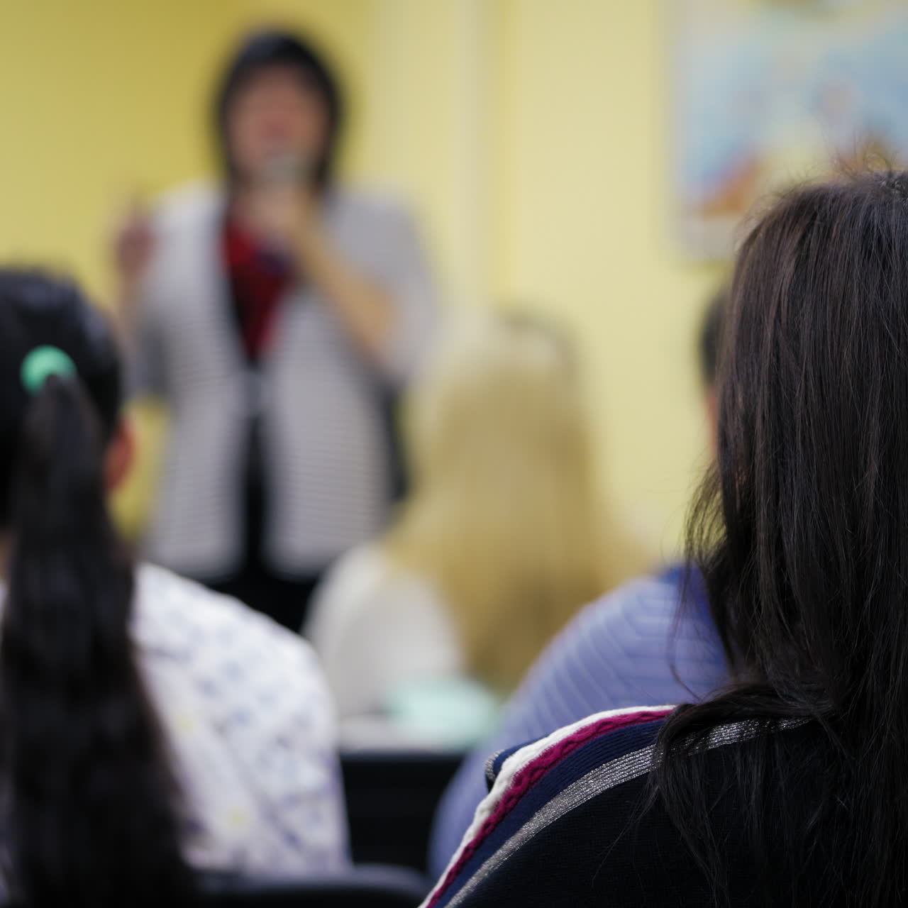 Back view of dark-haired female sitting in the conference hall on the blurred background. Young ladies sit and listen carefully to business training on women's development.