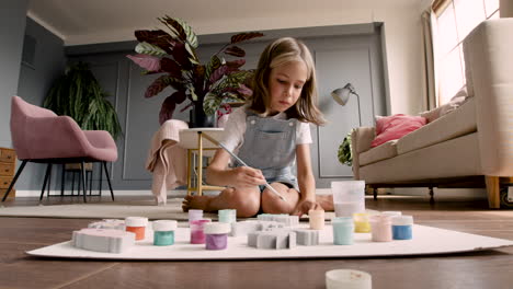 front view of blonde girl sitting on the floor and painting in living room