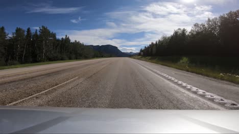 a pov shot of a car driving down an empty road towards the mountains