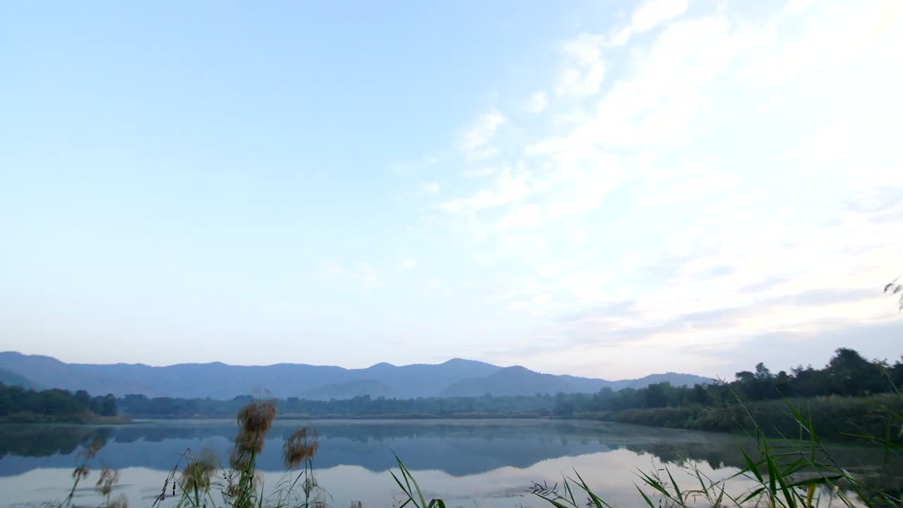A wide angle sunrise shot taking in a secluded lake found in Kanchanaburi, Thailand with clouds moving in and mist moving across the water