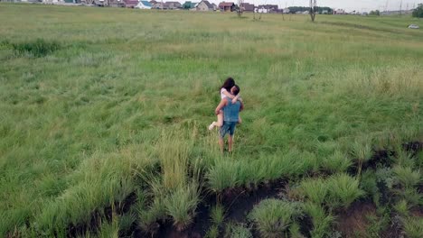 upper view brunette girl jumps into man arms on green meadow