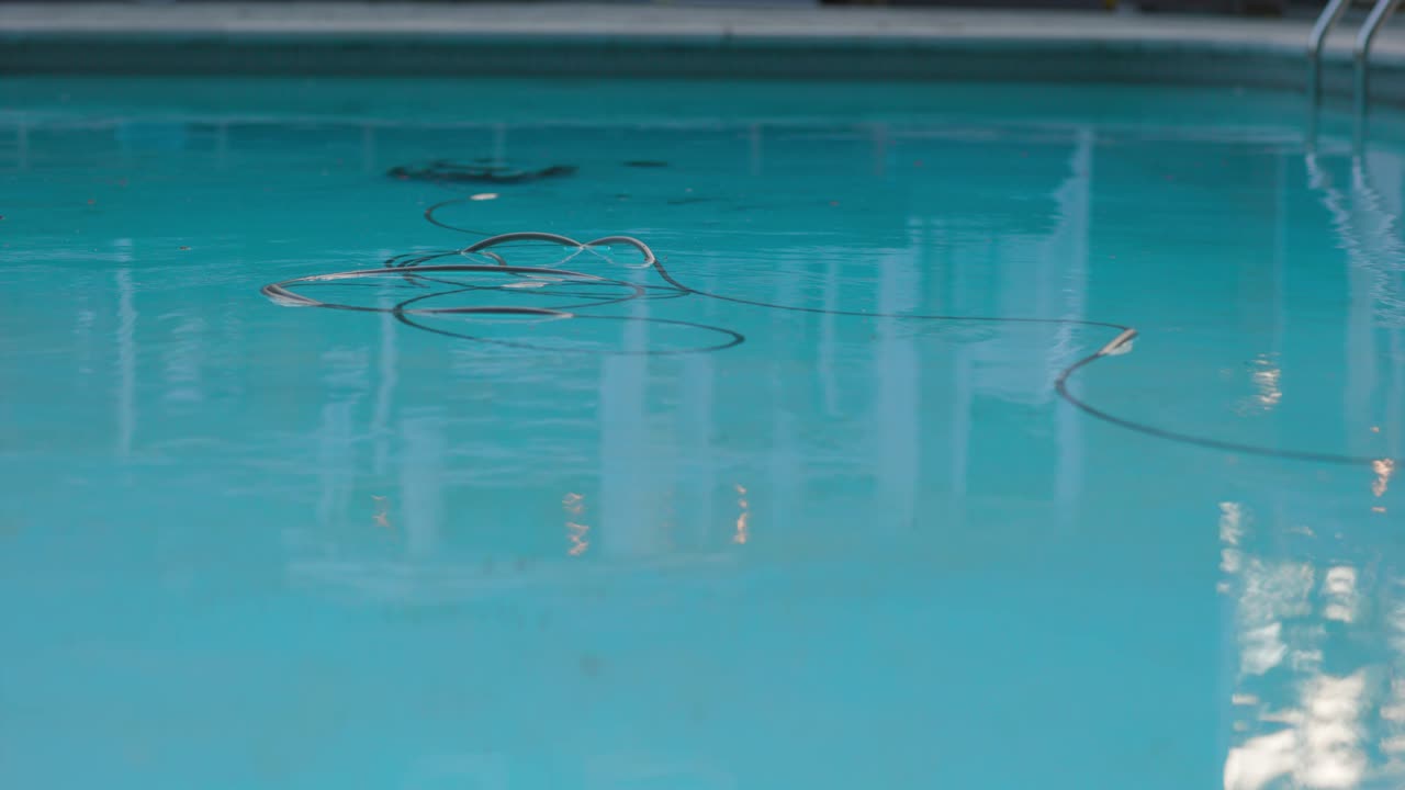 전기 수영장 청소 로봇은 깨끗한 반사 물에 떠 있는 전원 케이블로 멀리 있는 수영장을 청소합니다.