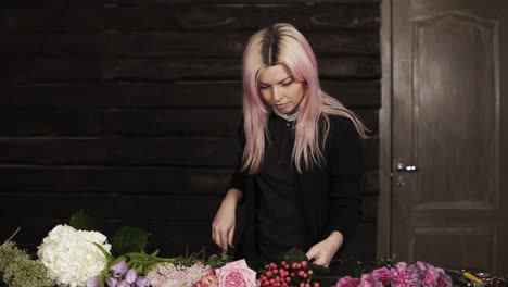 a charming florist with pink hair sorts out the flowers on the table, selects them for the future flower arrangement