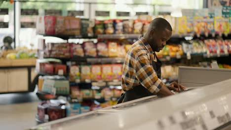 a man with black skin color in a plaid shirt sorts products in a supermarket refrigerator. video filmed in high quality