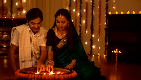 south indian couple in traditional wear lighting a lamp - diwali concept