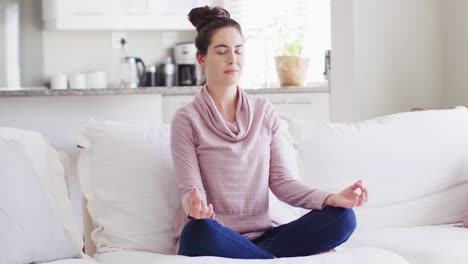 Happy-caucasian-woman-sitting-on-couch-and-meditating-in-living-room