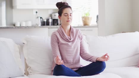 happy caucasian woman sitting on couch and meditating in living room